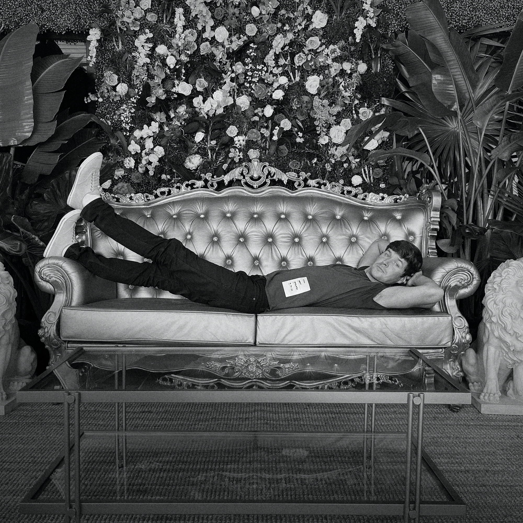 Man laying on ornate couch with floral backdrop during a film production.
